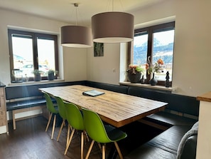 Ein Essbereich mit einem Holztisch, grünen Stühlen und Pendelleuchten.