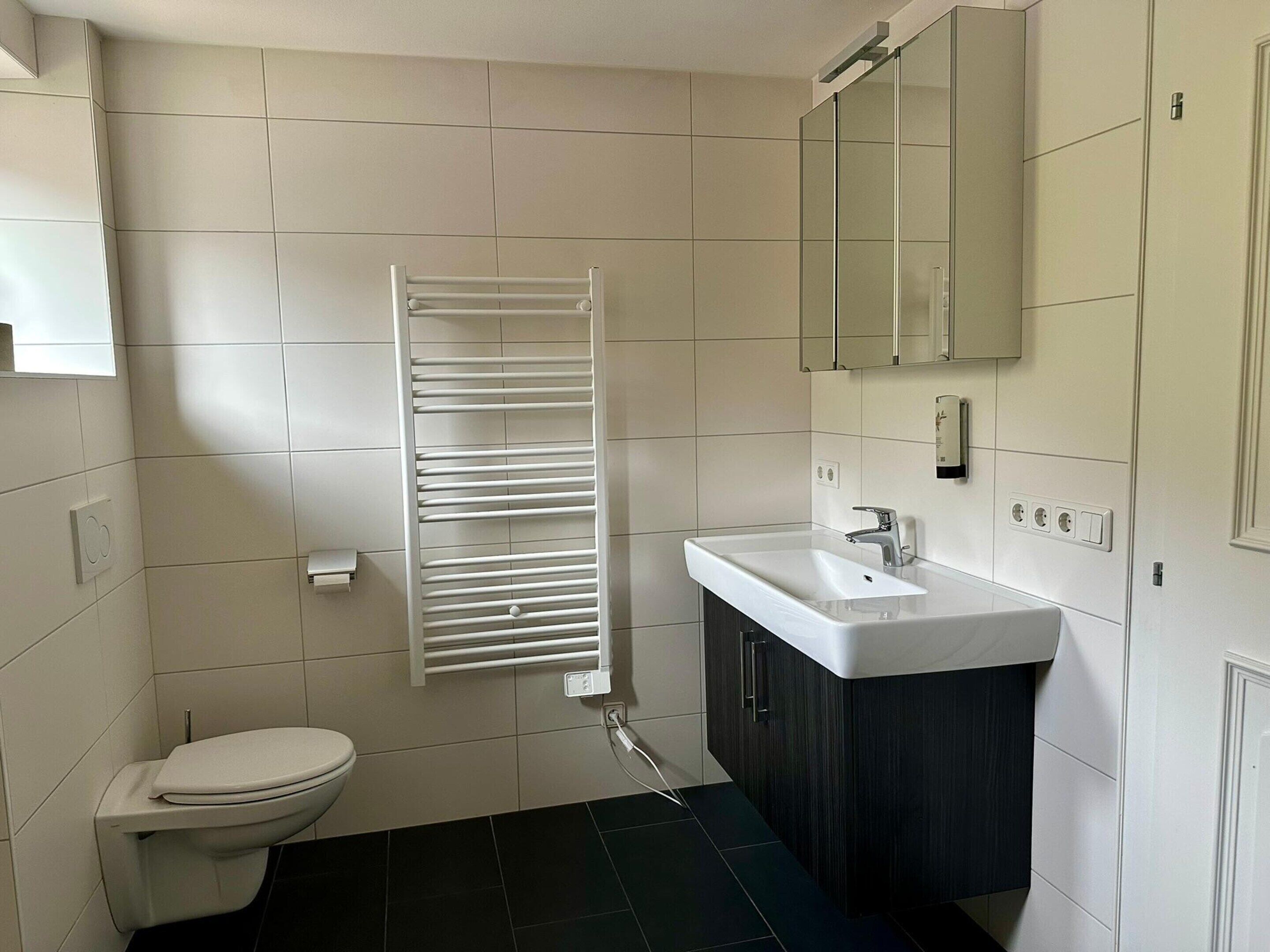 Une salle de bain comprenant des toilettes, un lavabo blanc, un miroir et un porte-serviettes.
