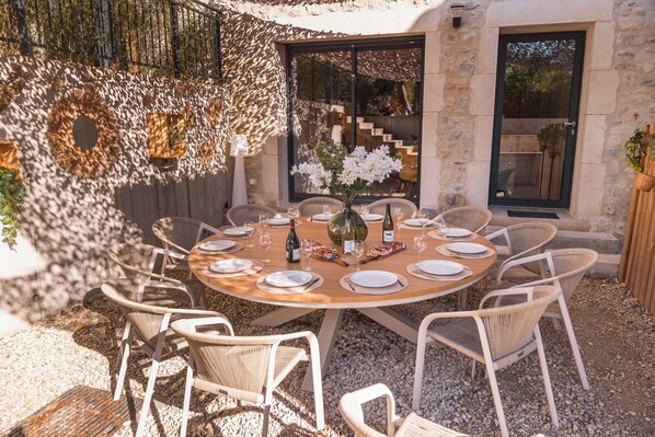 An outdoor dining area with a round table, wicker chairs, and a stone wall backdrop.