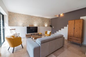 Un salon moderne avec un canapé, des fauteuils, un téléviseur et un escalier.