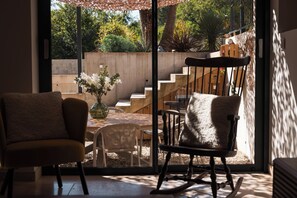 Une pièce dotée d’une grande porte-fenêtre coulissante qui donne sur un patio aménagé avec une chaise, une petite table et un pot de fleurs.