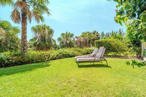 Un jardín con césped, palmeras y una silla de descanso.