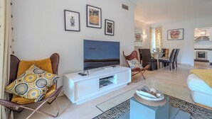 A modern living room with a flat-screen TV, a white entertainment unit, and a dining area with chairs and a table. - Lalq13 Stunning Frontline Golf 3 bed apt (Benahavis)