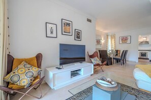 A modern living room with a flat-screen TV, a white entertainment unit, and a dining area with chairs and a table. - Lalq13 Stunning Frontline Golf 3 bed apt (Benahavis)
