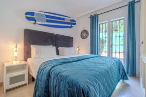 Un dormitorio con una cama, una mesita de noche, un reloj de pared y una ventana con cortinas.