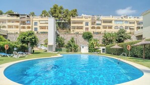 A swimming pool with lounge chairs and umbrellas, surrounded by a stone wall and greenery. - Lalq13 Stunning Frontline Golf 3 bed apt (Benahavis)