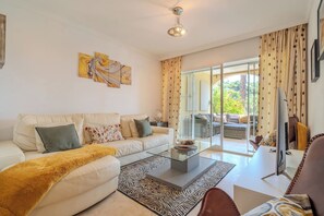 A modern living room with a sofa, coffee table, and a view through a glass door. - Lalq13 Stunning Frontline Golf 3 bed apt (Benahavis)