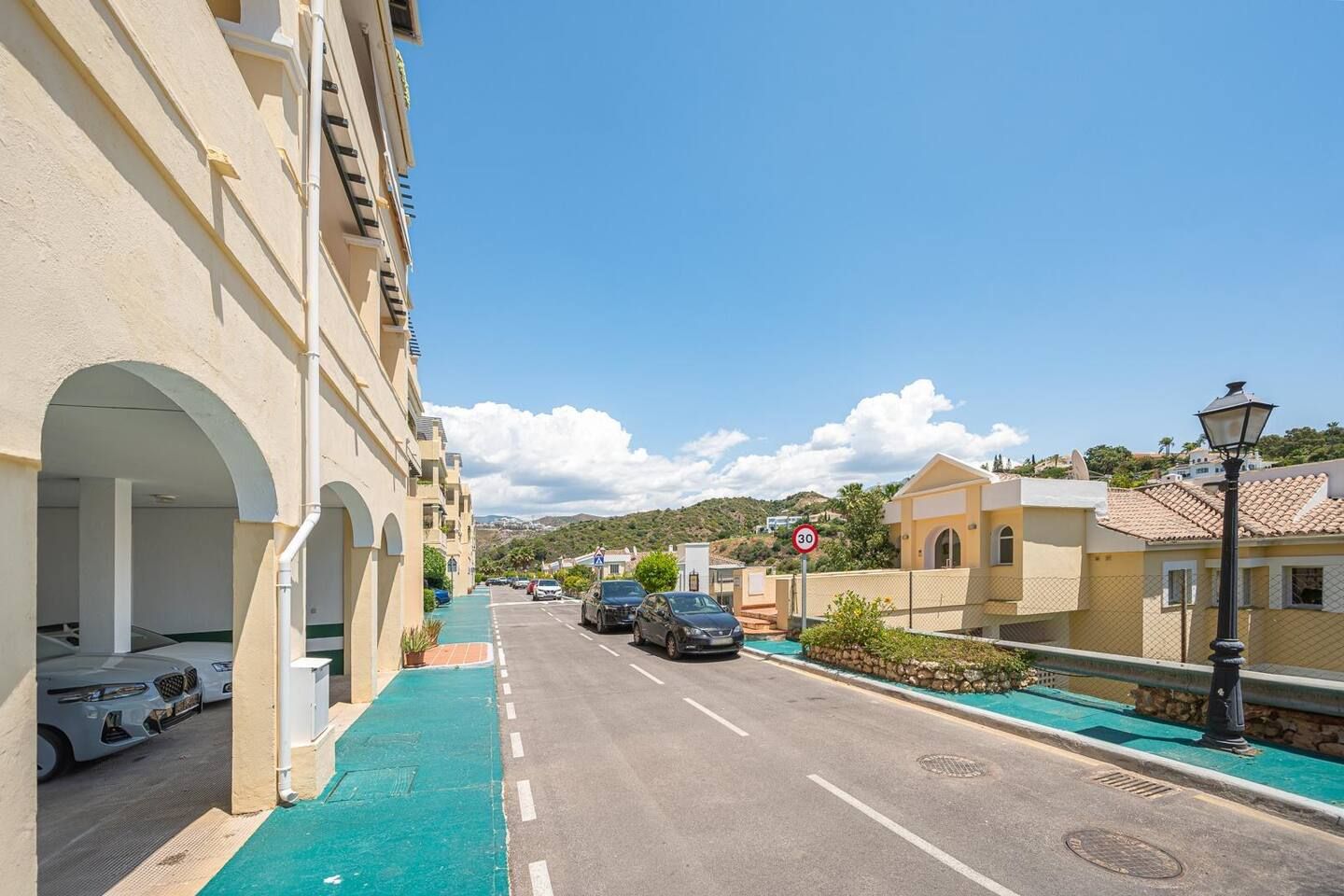 A street with parked cars, a speed limit sign, and buildings with balconies.