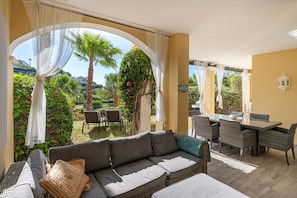 A sunlit outdoor seating area with a sofa, chairs, and a dining table.