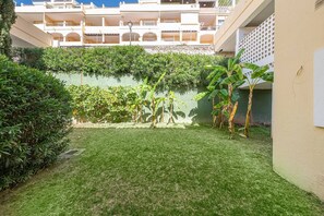 A courtyard with a grassy area, a green wall, and a building with multiple balconies in the background. - Lalq13 Stunning Frontline Golf 3 bed apt (Benahavis)