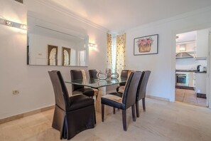 A dining area with a glass table and black chairs, a kitchen in the background, and a mirror on the wall. - Lalq13 Stunning Frontline Golf 3 bed apt (Benahavis)