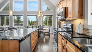 A modern kitchen with a large island, wooden cabinets, and a view of the outdoors. - Evercrest A-Frame | Hot Tub | Pool Tbl | Fireplace (Radium Hot Springs)