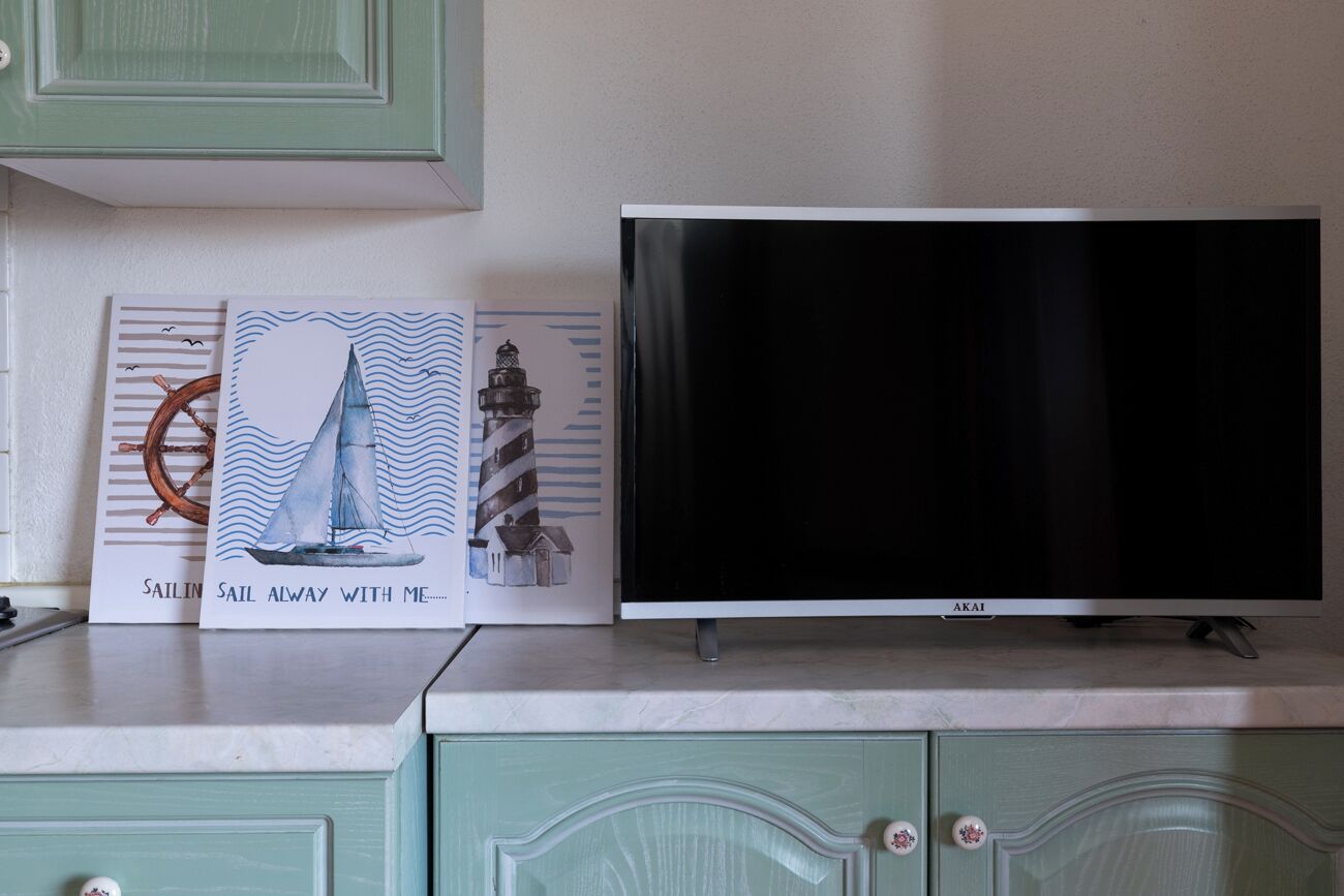 A flat-screen TV on a cabinet, with two framed artworks depicting sailing scenes.