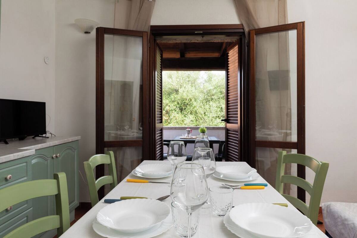 A dining table set with plates, glasses, and cutlery, with a television on a cabinet to the left.