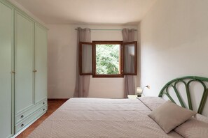 Une chambre à coucher avec un lit, une armoire, une fenêtre avec des rideaux et une table de chevet avec une lampe.