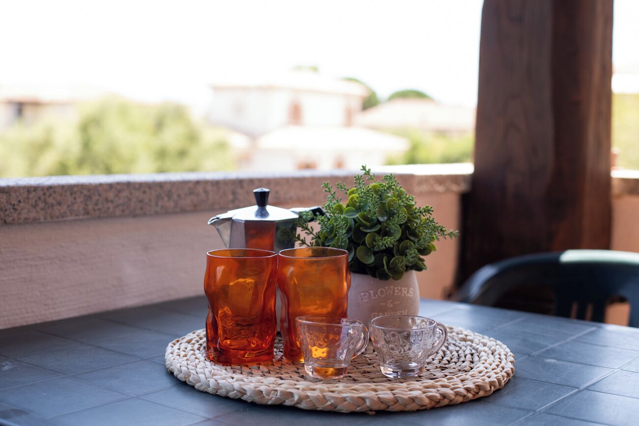 Une table avec un set de table en fibres tressées, une cafetière et une plante en pot, le tout sur un balcon offrant une vue.