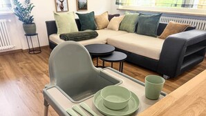 A modern living room with a sofa, a dining area with a table and chairs, and a potted plant.