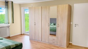 A bedroom with a large wardrobe, a bed, and a window with a view of greenery.