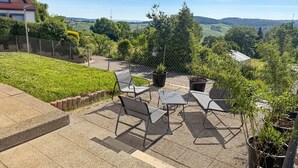A patio with outdoor furniture and potted plants, overlooking a rural landscape.