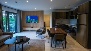 Een moderne woonkamer met een televisie, bank, salontafel en een eethoek.