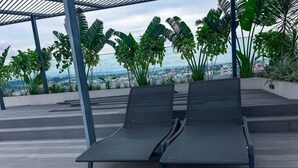 Twee comfortabele stoelen op een houten terras met uitzicht op een stadsbeeld.