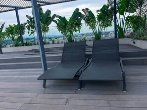 Zwei Liegestühle auf einer Holzterrasse mit Blick auf eine Stadtlandschaft.