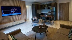 Een moderne woonkamer met een flatscreen televisie, een eethoek en een keuken.