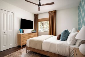 Ein Schlafzimmer mit Bett, Deckenventilator, Fernseher, Fenster mit Vorhängen und Nachttisch.