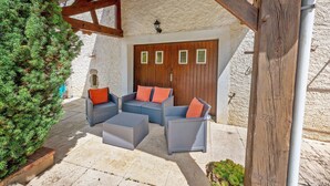 An outdoor seating area with wicker furniture and cushions, a wooden door with windows, and a stone wall.