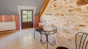 A room with a stone wall, a wooden door, a radiator, a round metal table with chairs, and a patterned wall.