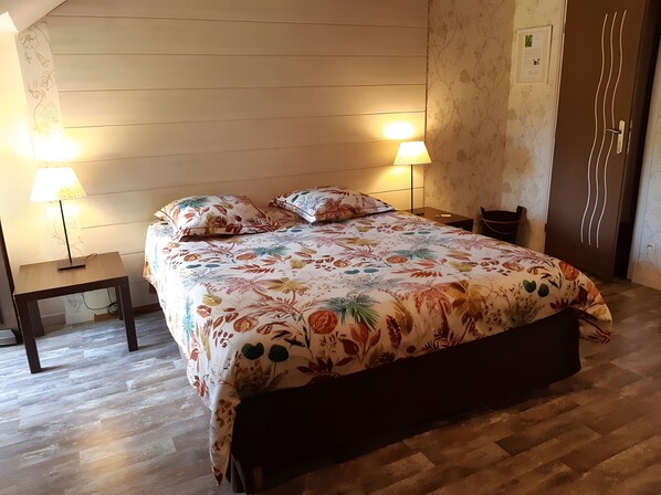Une chambre à coucher avec une couvre-lit à motifs floraux, deux lampes de chevet, une table de chevet en bois et un plancher en bois.