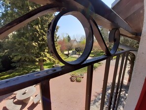 A metal railing with a circular design, a paved path, and greenery in the background.