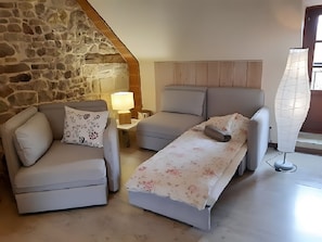 A room with a stone wall, a sofa, a daybed, a lamp, and a window.