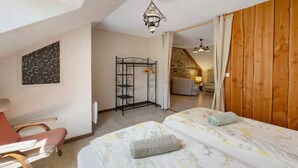 A room with two beds, a chair, a radiator, a hanging light fixture, and a wooden wall.