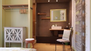A bedroom with a bed, a wardrobe, a chair, a mirror, and a bathroom with a sink and mirror.