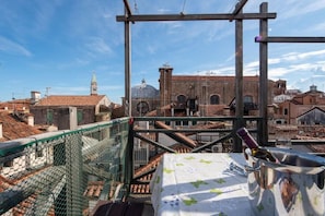 Eine Dachterrasse mit Blick auf historische Gebäude, einem Metallgeländer und einem Tisch mit einer Flasche.