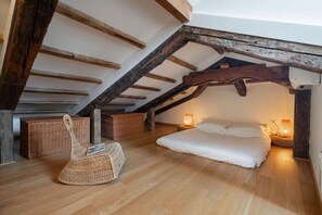 Ein gemütliches Schlafzimmer im Dachgeschoss mit freiliegenden Holzbalken, einem Bett, zwei Korbwannen und einem gewebten Stuhl.
