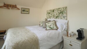 A bedroom with a bed, a nightstand, a coffee maker, a framed picture, and a wooden hanger rack. - Tracey Cottage (Newton Abbot)