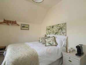 A bedroom with a bed, a nightstand, a coffee maker, a framed picture, and a wooden hanger rack. - Tracey Cottage (Newton Abbot)