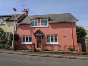 A two-story house with a red exterior, a front door, and a small porch. - Tracey Cottage (Newton Abbot)