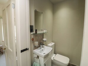 A bathroom with a white sink, a toilet, a mirror, and a glass shelf with toiletries. - Tracey Cottage (Newton Abbot)
