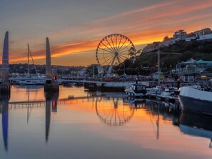 A waterfront marina with boats, a Ferris wheel, and a prominent tower. - Tracey Cottage (Newton Abbot)