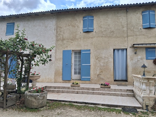 Un bâtiment doté d’une façade en pierre, de volets bleus et d’un petit porche avec des marches menant à l’entrée.