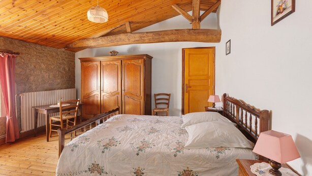 Ein Schlafzimmer mit einem hölzernen Bett, einem Schrank aus Holz, einem Sessel, einem Schreibtisch und einer Heizung.