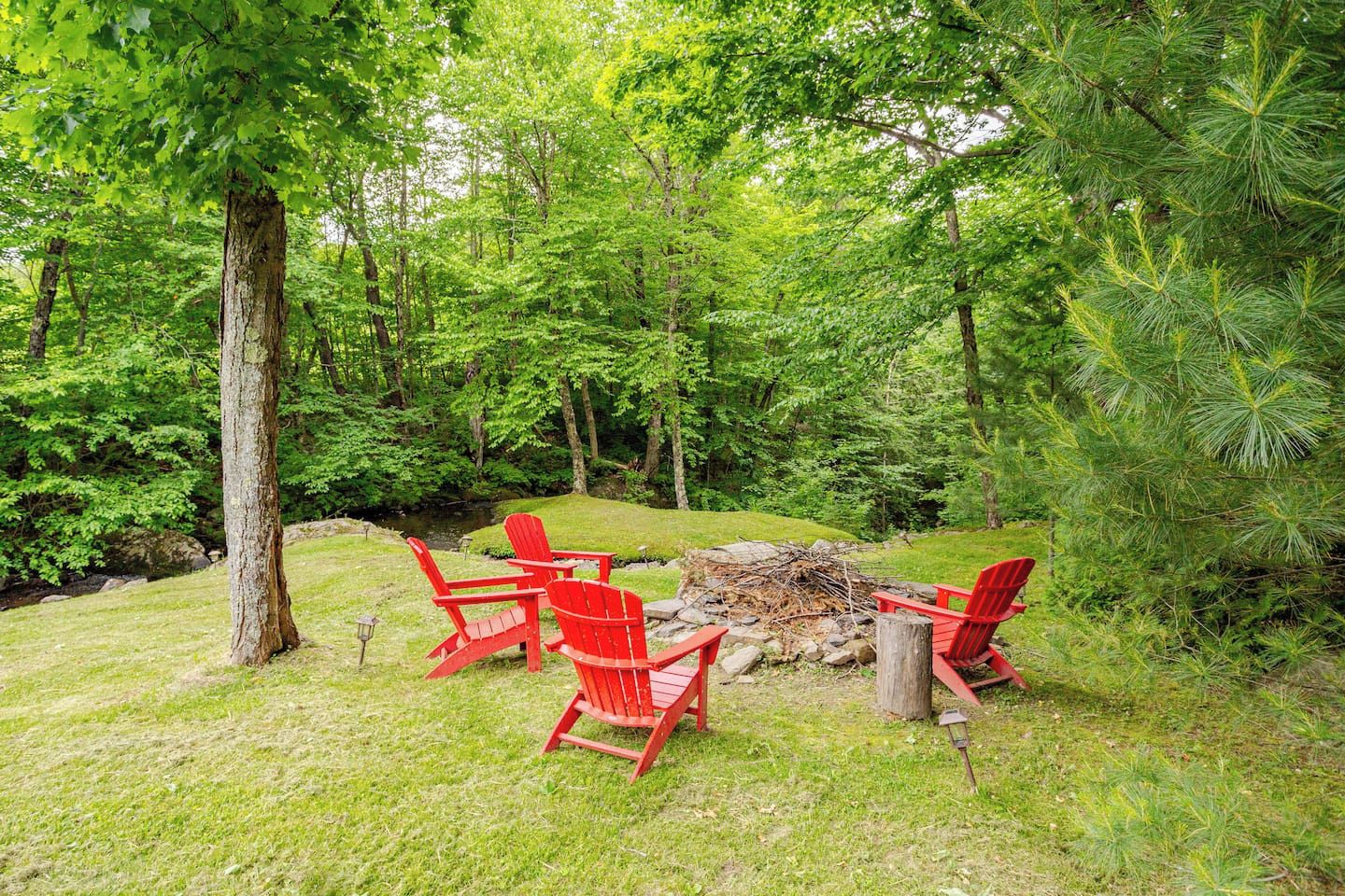 Un espace extérieur aménagé avec des chaises rouges et un foyer, le tout entouré d’une végétation luxuriante.