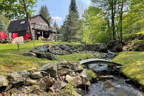 Eine rustikale Holzhütte mit einer Veranda, eingebettet in eine natürliche Landschaft mit Bach und Felsen.