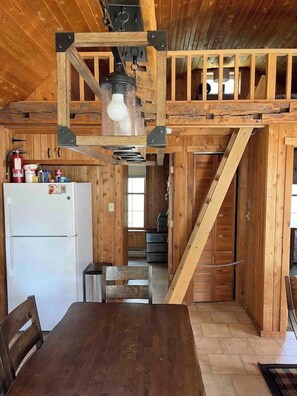 Interior de fusta amb zona de cuina, taula de dinar i escala.