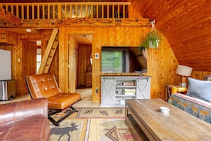 A wooden interior with a TV, leather chair, sofa, and a staircase.