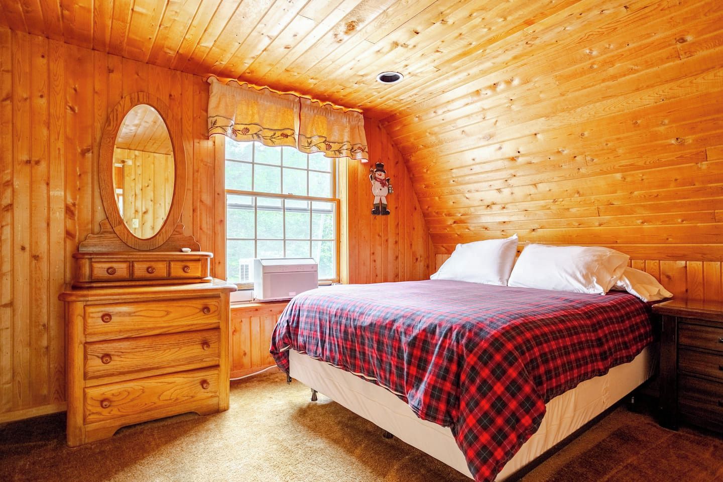 Une pièce aux murs lambrissés, comprenant un lit, une commode et une fenêtre avec des rideaux.
