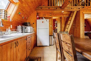 A wooden cabin interior with a kitchen area, including a refrigerator, microwave, and wooden cabinets.